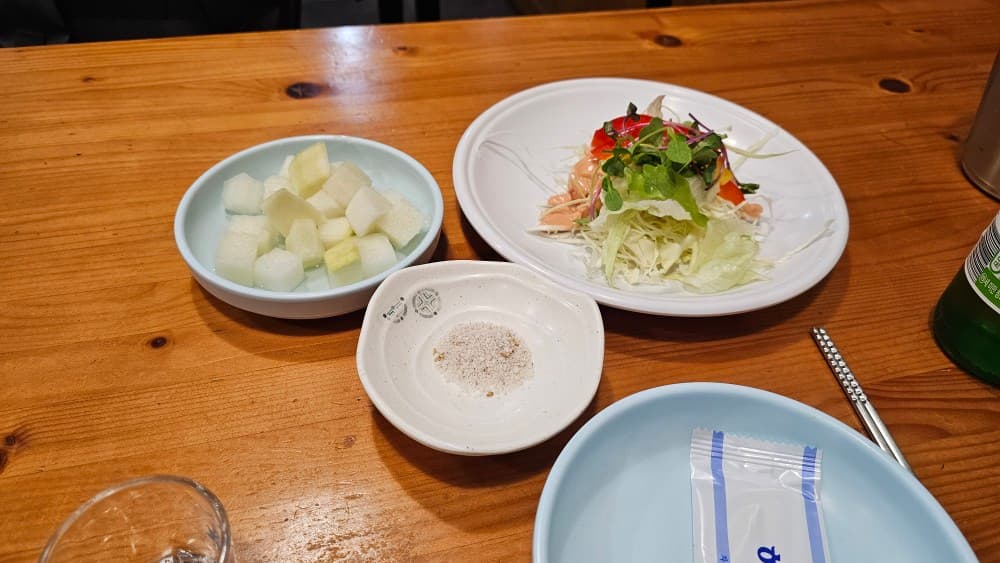 부산광역시 연제구 혼술 치킨 닭강정 초원통닭 부산시청 - 나무 테이블 위 1인용 양배추 샐러드와 치킨무, 소금이 놓인 기본 식사 차림 상황