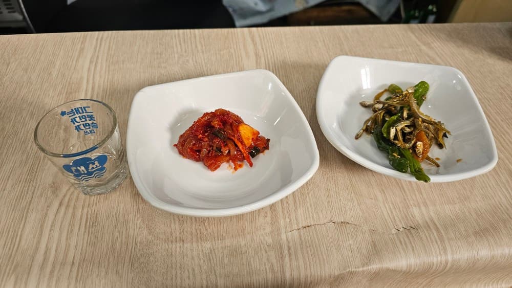 부산광역시 동구 신촌포차 초량 포장마차 밝은 조명 아래 나무 카운터석과 대선 소주잔, 멸치 볶음, 양념 무침. 1인 혼술 다찌석 상차림