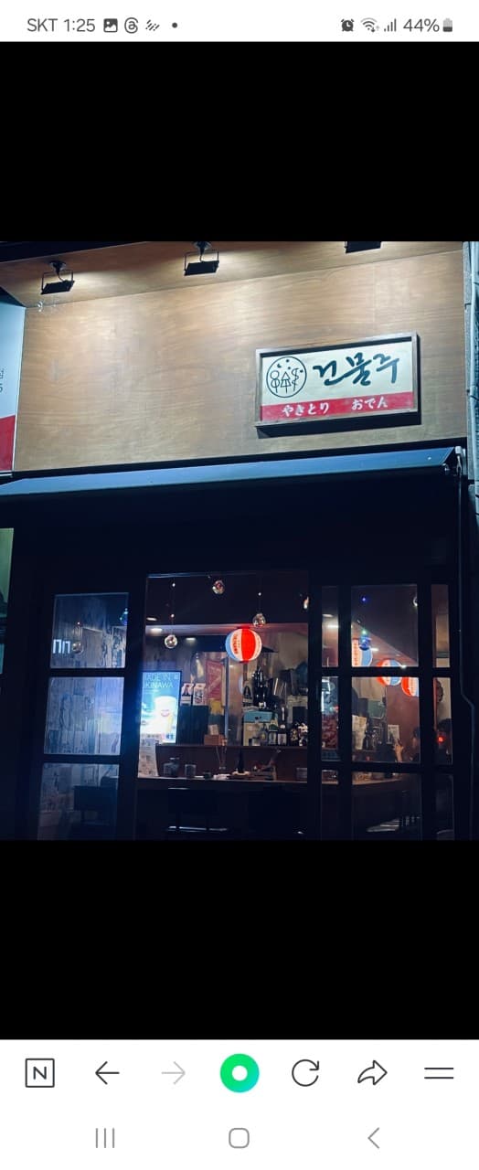 경기도 의정부시 오뎅바 건물주 - 목재 외벽 아래 붉은 제등과 1인 다찌석이 위치한 실내. 혼술을 위한 바 테이블과 진열된 주류 병들이 보이는 밤 시간의 전경