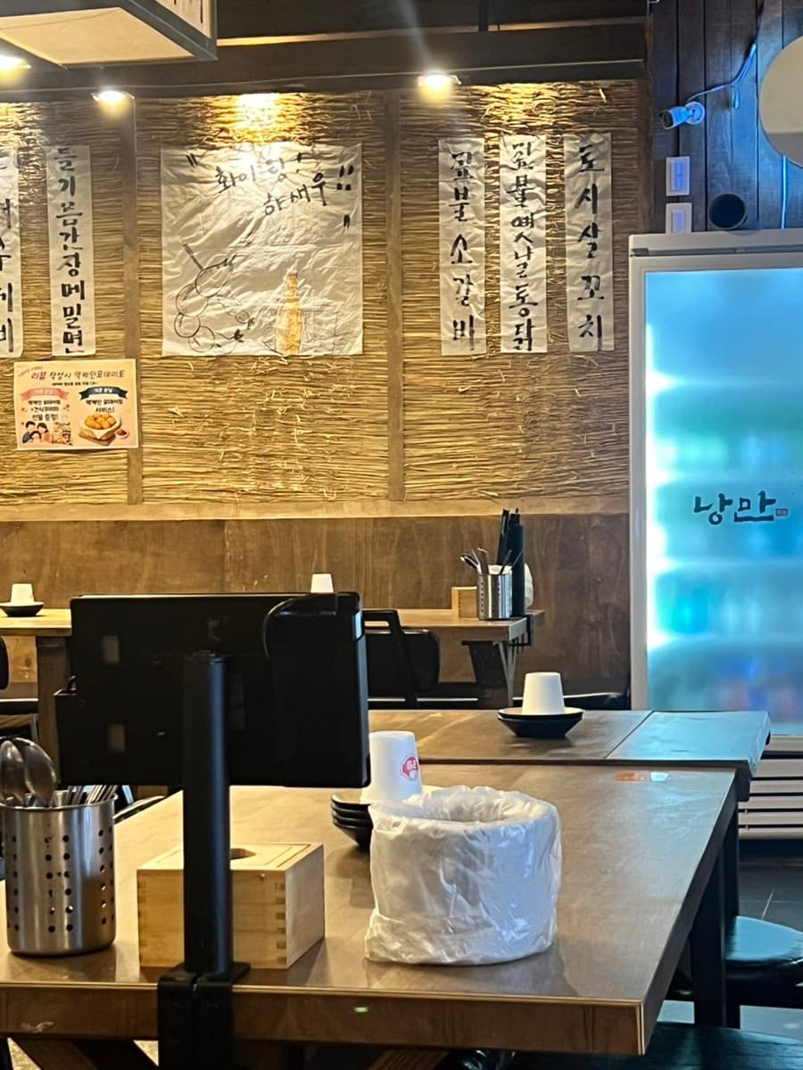 경기도 광주시 낭만짚불구이 경안점 요리주점. 짚불 메뉴가 붙은 벽면과 핀 조명 아래 1인 태블릿 좌석이 비치된 테이블에서 혼술을 즐기는 상황.