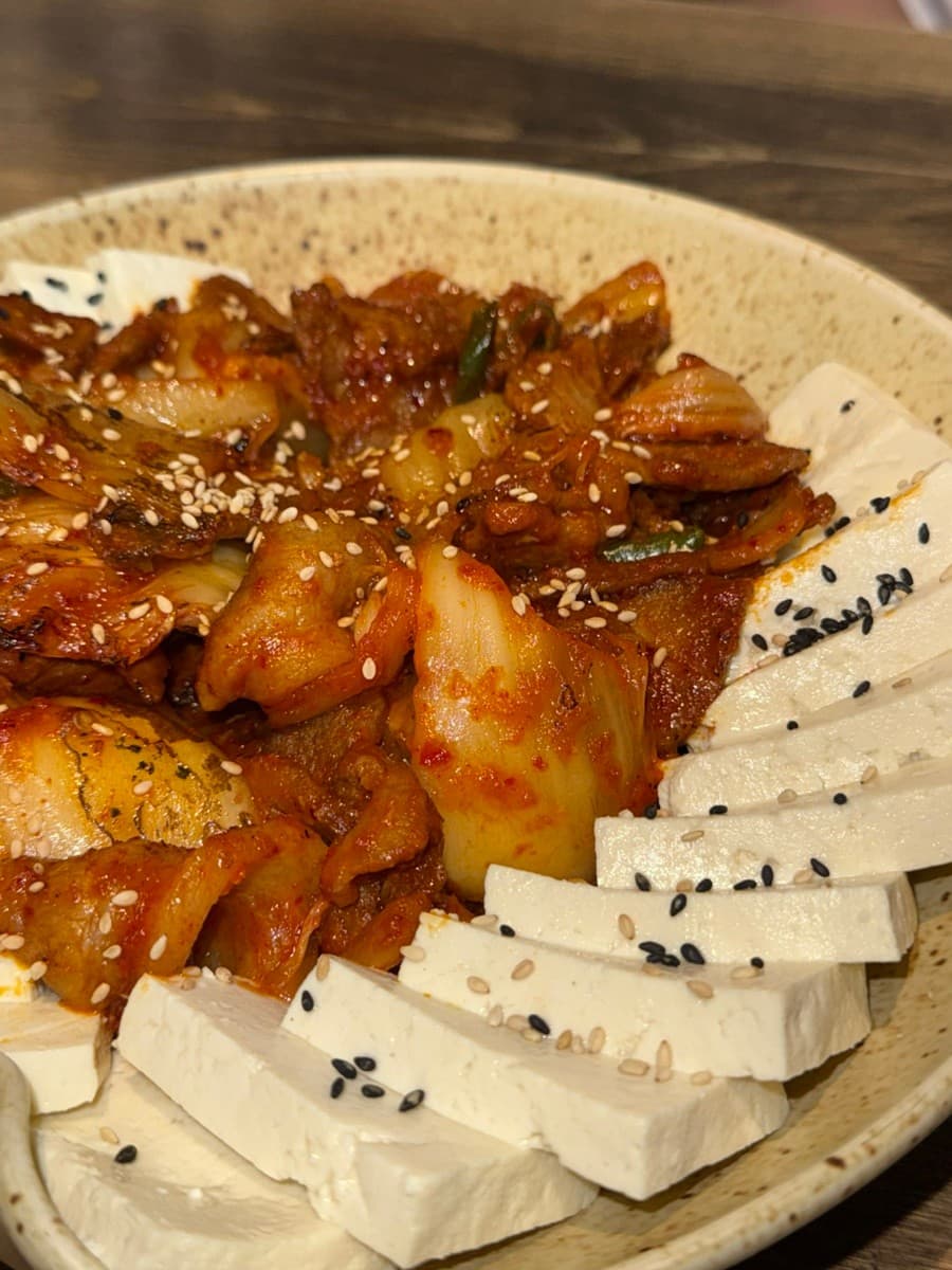 경기도 광주시 요리주점 낭만짚불구이 경안점 1인 다찌석 혼술. 조명 아래 참깨가 뿌려진 두부와 김치제육볶음이 나무 테이블 위 접시에 담긴 모습.