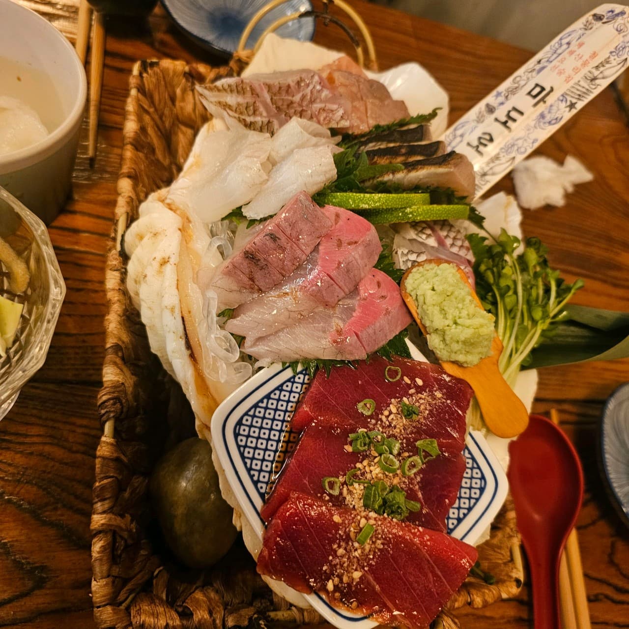 경기도 광주시 이자카야 마도로쓰 다찌석 1인 사시미. 주황빛 조명 아래 참치와 활어회가 담긴 바구니. 와사비와 무순을 곁들여 목재 테이블에서 혼술을 즐기는 상황.