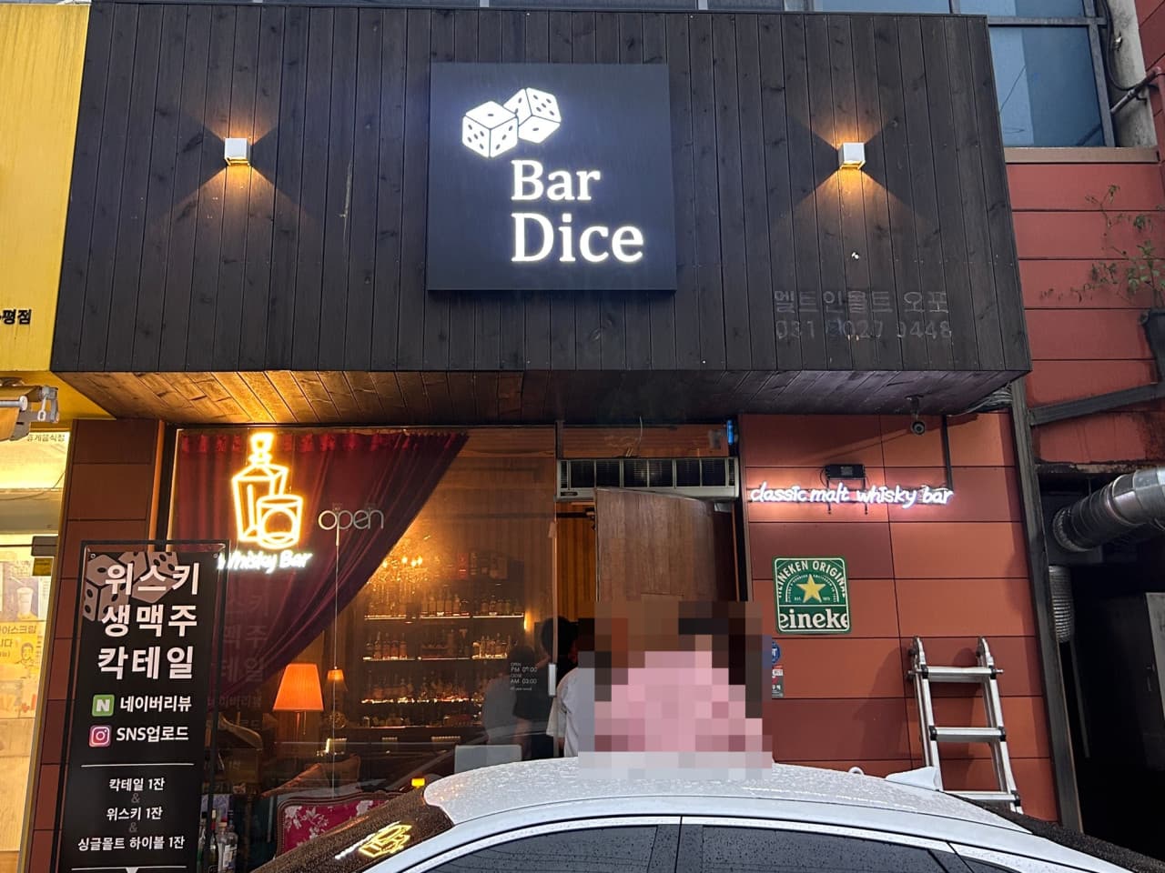 경기도 광주시 다이스 바(Bar) - 어두운 목재 외벽에 황색 조명이 켜진 입구와 유리창 안으로 위스키 병이 진열된 다찌석이 보이는 혼술 상황