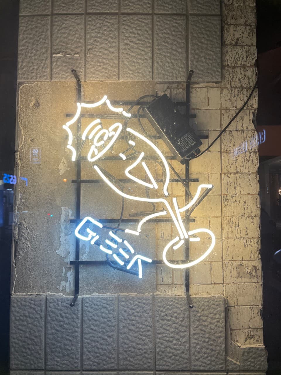 대구광역시 중구 와인바 긱 대구 입구의 와인잔 캐릭터 네온사인 조명. 거친 질감의 타일 벽면과 대비되는 밝은 빛이 혼술 또는 1인 와인을 즐기는 상황을 나타냄.