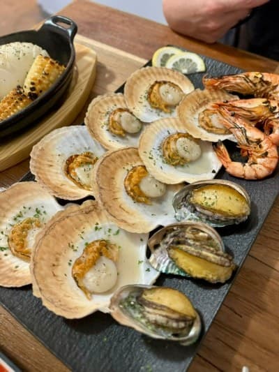 대구광역시 중구 혼술 요리주점 대구 수상한한옥집 - 조명 아래 다찌석에 가리비와 전복, 새우 구이가 1인 상차림으로 차려져 해산물의 질감이 돋보임