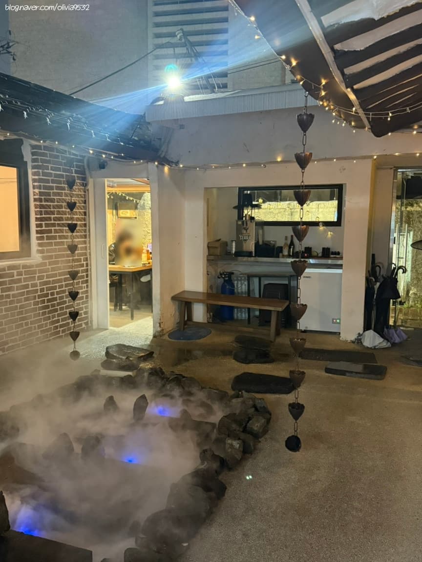 대구광역시 중구 요리주점 대구 수상한한옥집 - 푸른 조명과 안개가 깔린 연못 앞 목재 벤치. 낙수 체인이 내려온 처마 아래 다찌석이 보이는 1인 혼술 공간.