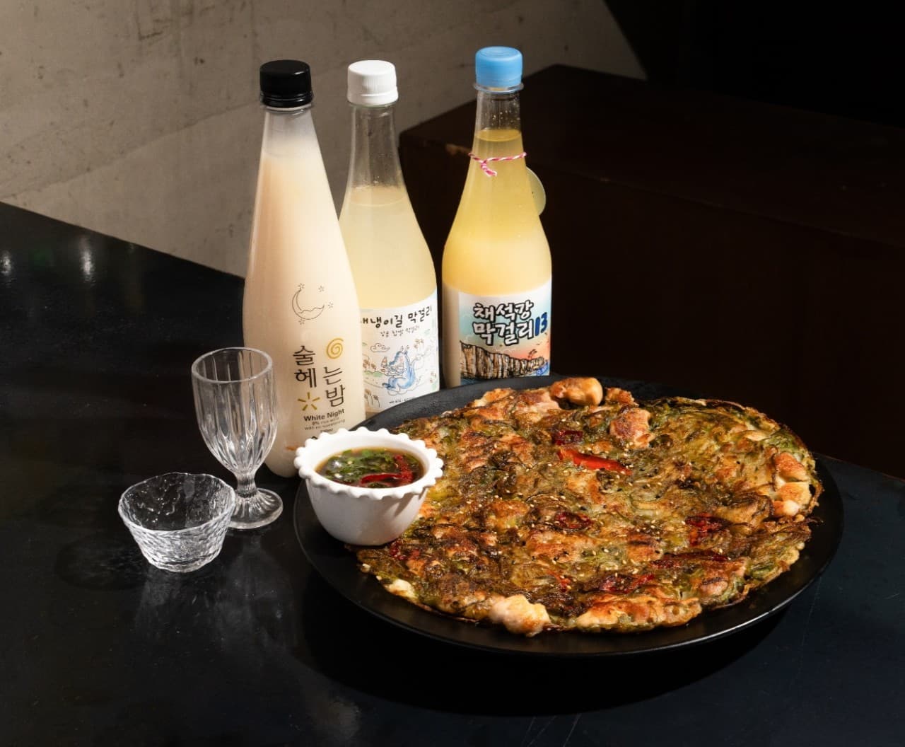 대구광역시 중구 전통주점 활력 다찌석에 차려진 노릇한 전과 막걸리. 조명을 받아 질감이 강조된 1인 혼술 상차림과 투명한 술잔이 놓인 테이블.