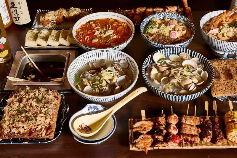 전남광주통합특별시 목포시 오니 본점 전남 이자카야 다찌석 1인 혼술 차림. 조명 아래 꼬치구이와 조개탕, 가쓰오부시가 뿌려진 요리들이 나무 테이블 위에 배치된 상황.