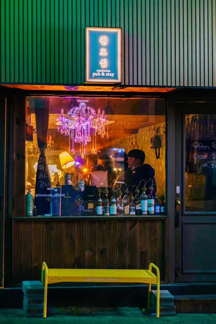 전남광주통합특별시 목포시 원도심펍 전남 이자카야 외관. 샹들리에 조명 아래 다찌석과 진열된 술병들, 입구 앞 노란 벤치가 있는 혼술 공간.