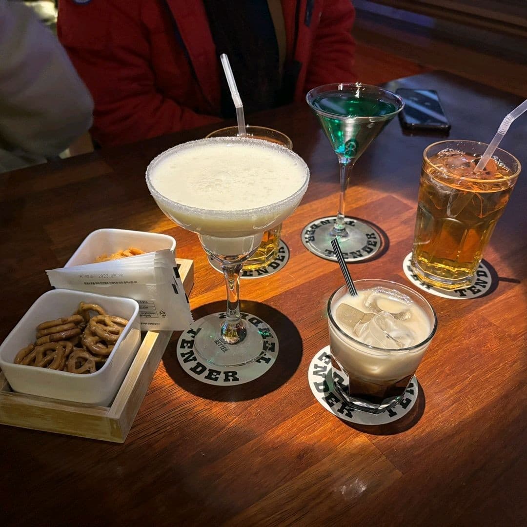 전남광주통합특별시 순천시 텐더 전남 바(Bar)의 핀 조명 아래 놓인 설탕 림 칵테일과 프레첼. 목재 다찌석에서 1인 혼술을 즐기는 상황.