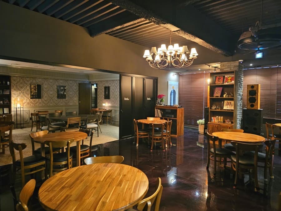 전남광주통합특별시 순천시 바(Bar) 펜스터 전남 내부. 샹들리에 조명 아래 원목 테이블과 혼술용 1인석이 배치된 공간. 광택 있는 바닥에 빛이 반사되며 레코드판과 스피커가 진열됨.