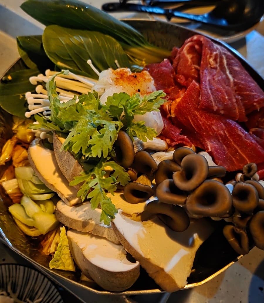 전남광주통합특별시 순천시 무카 전남 이자카야 다찌석에 놓인 1인 전골. 선홍빛 소고기와 버섯의 질감이 돋보이며 조명 아래 혼술을 즐기는 상황.
