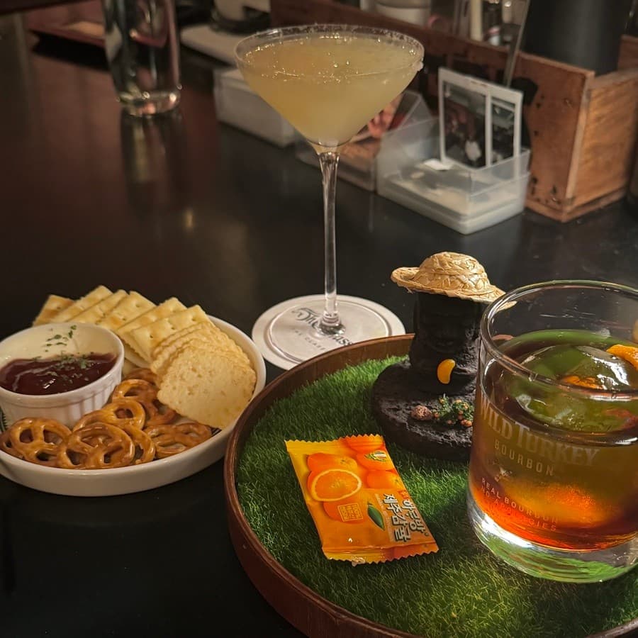 전남광주통합특별시 순천시 더클래식 전남 바(Bar) - 다찌석 조명 아래 마티니와 위스키, 크래커 안주가 차려진 1인 혼술 테이블 구성