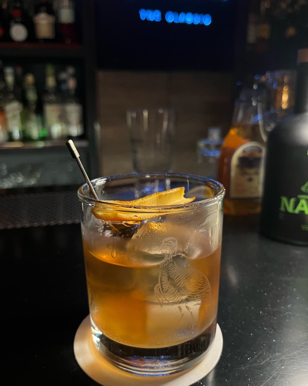 전남광주통합특별시 순천시 바(Bar) 더클래식 전남 다찌석에 놓인 위스키 칵테일. 어두운 조명 아래 큰 얼음과 오렌지 껍질이 담긴 유리잔이 1인 혼술 상황을 보여줌.
