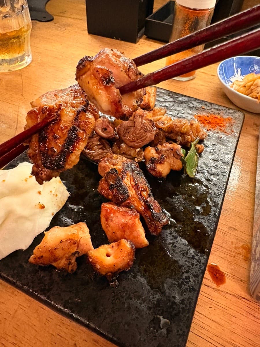 인천광역시 남동구 요리주점 하나마토 구월 인천 1인 다찌석. 조명 아래 육즙 가득한 닭구이와 양배추가 차려진 검은 석판 위 나무 젓가락으로 고기를 집는 혼술 상황.