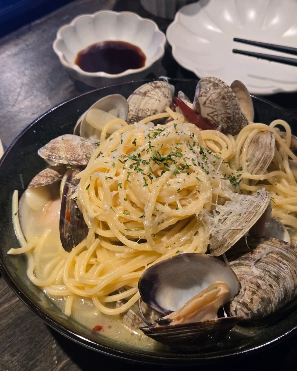 인천광역시 남동구 이자카야 물고기골목 인천 다찌석. 조명 아래 치즈가루가 뿌려진 바지락 파스타와 간장 종지가 차려진 1인 혼술 테이블.