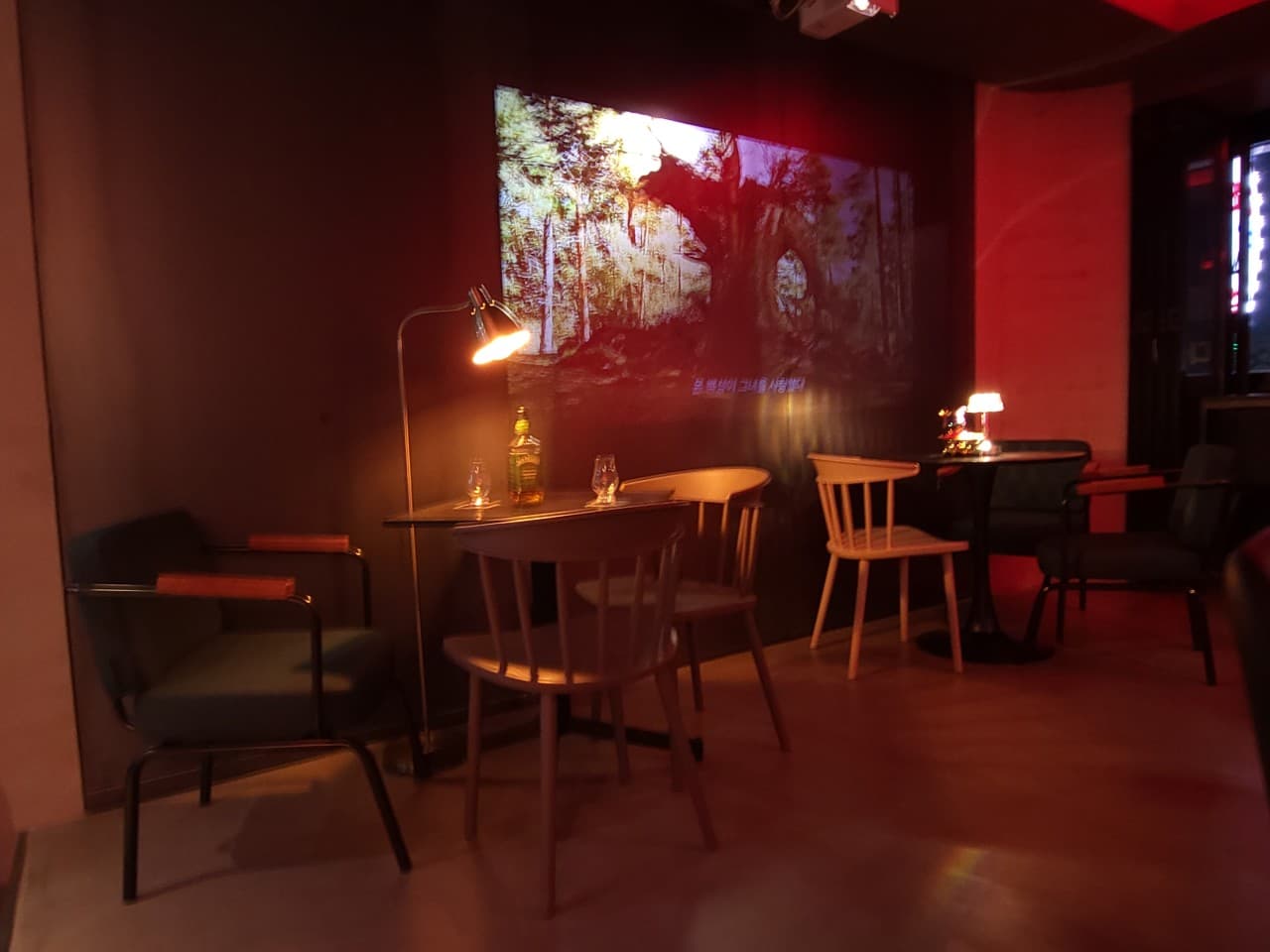 인천광역시 미추홀구 레이브 인천 바(Bar) - 빔 프로젝터 영상이 투사된 벽면과 스탠드 조명 아래 위스키 병이 놓인 테이블. 1인용 좌석이 배치된 어두운 조도의 공간에서 혼술을 하는 상황.