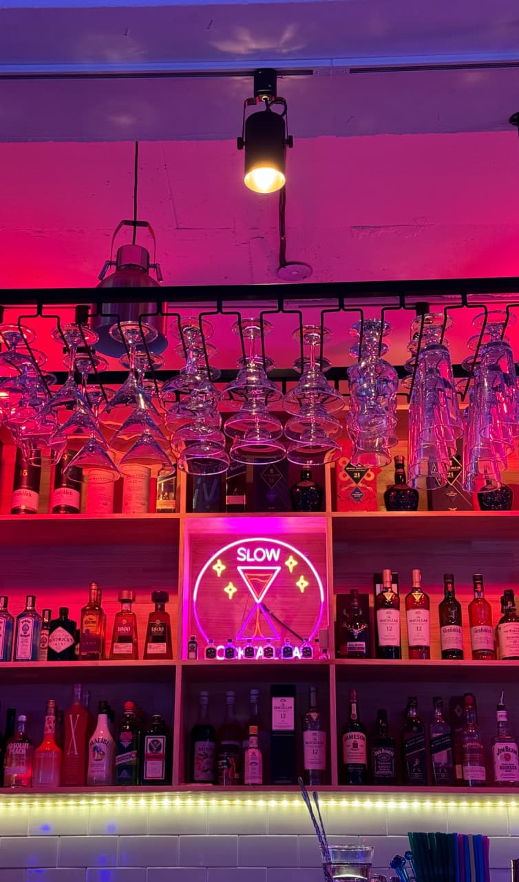 인천광역시 미추홀구 슬로우 인천 바(Bar)의 분홍색 네온 조명 아래 진열된 위스키와 유리잔. 혼술용 다찌석 정면으로 보이는 선명한 색감의 진열장과 칵테일 네온사인 전경.