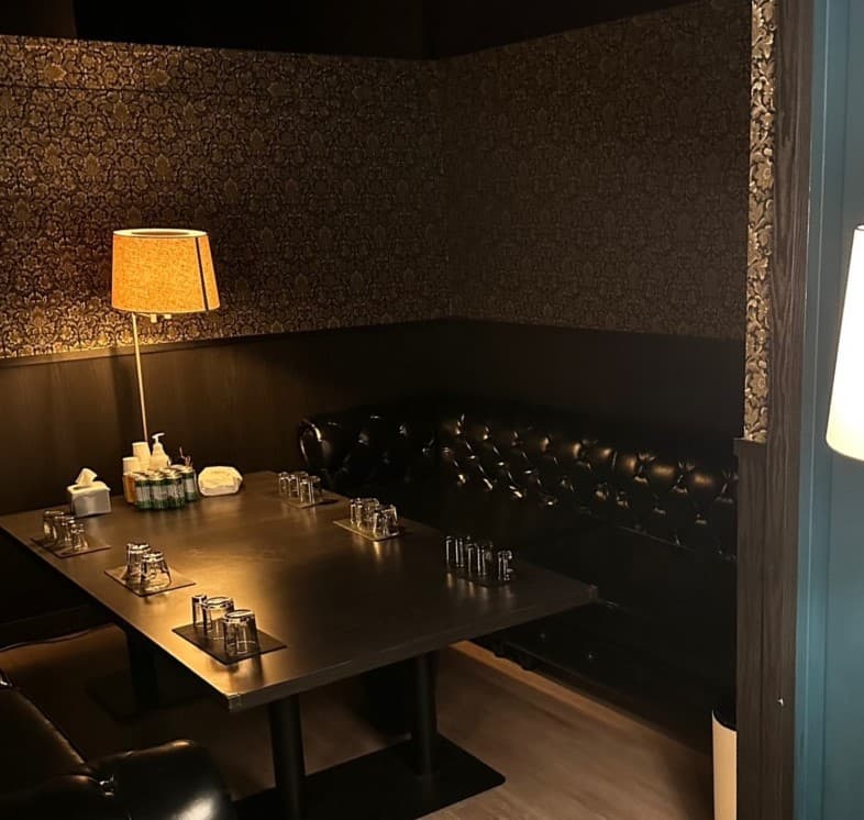 인천광역시 연수구 VIP BAR 인천 바(Bar)의 주황색 스탠드 조명과 블랙 가죽 소파. 테이블 위 나란히 놓인 유리잔과 1인 방문이 가능한 어두운 톤의 실내 전경.