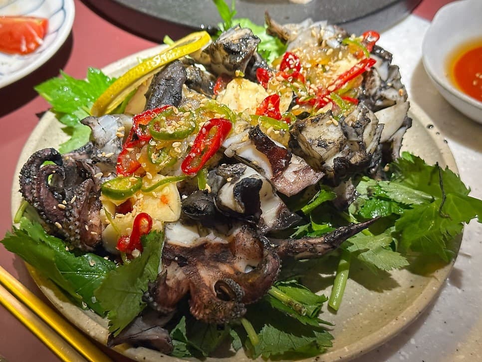인천광역시 부평구 요리주점 소담주택 인천 - 조명 아래 다찌석에 차려진 그릴 오징어와 채소. 고추가 올라간 해산물 질감이 보이는 1인 혼술 테이블.