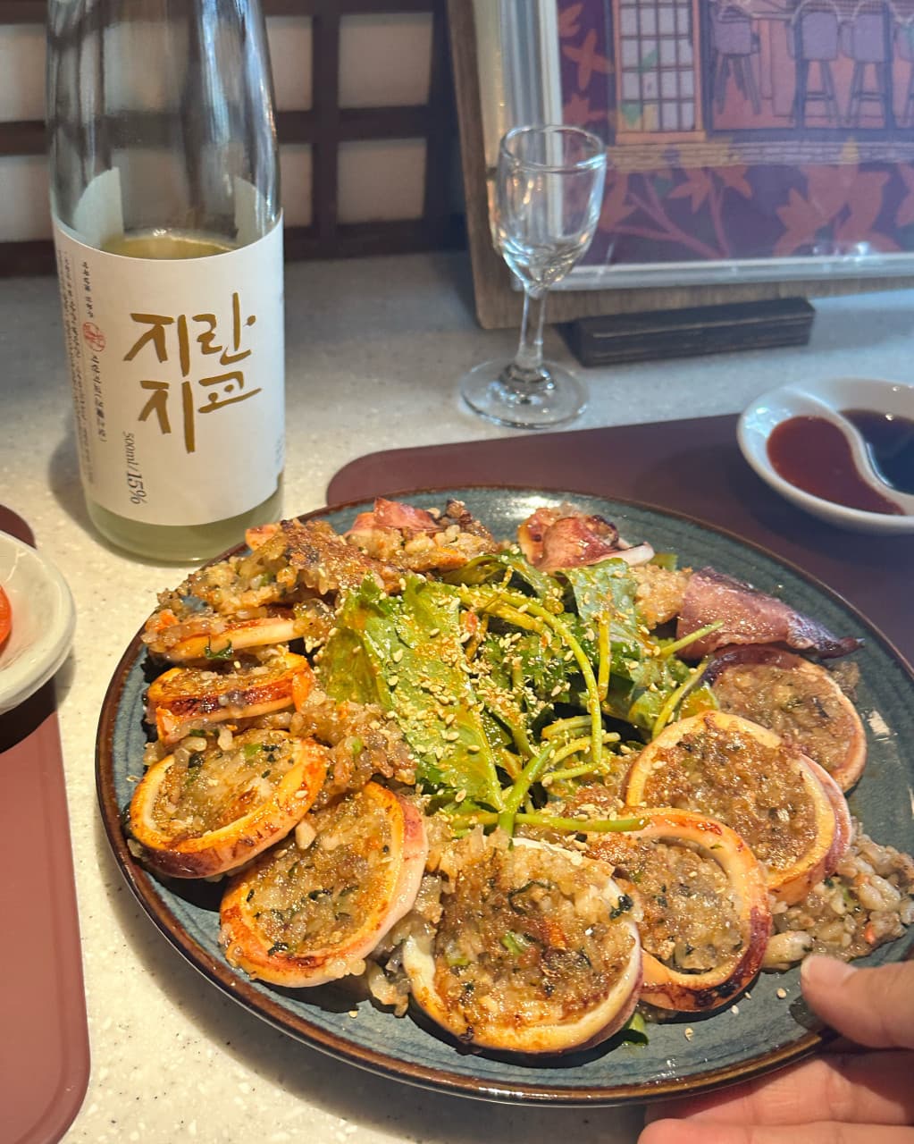 인천광역시 부평구 소담주택 인천 요리주점 다찌석 혼술. 지란지교 전통주와 속이 꽉 찬 오징어순대 요리가 놓인 1인 좌석과 나무 격자 칸막이의 조명 연출.