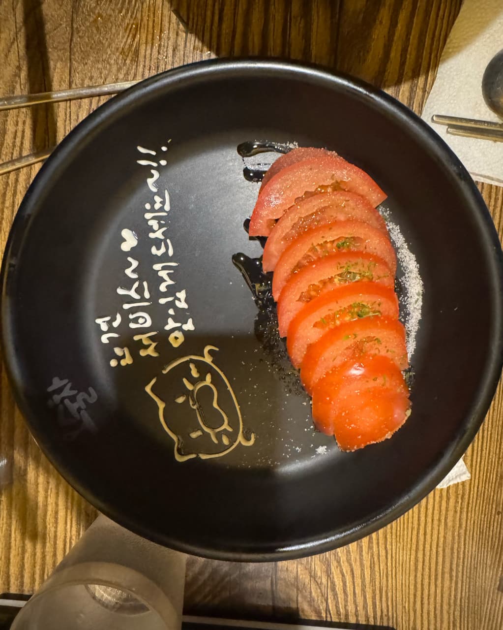 인천광역시 부평구 요리주점 오술차 부평역점 인천 - 조명 아래 다찌석 나무 테이블 위 설탕 뿌린 토마토와 손글씨 문구가 담긴 접시의 1인 혼술
