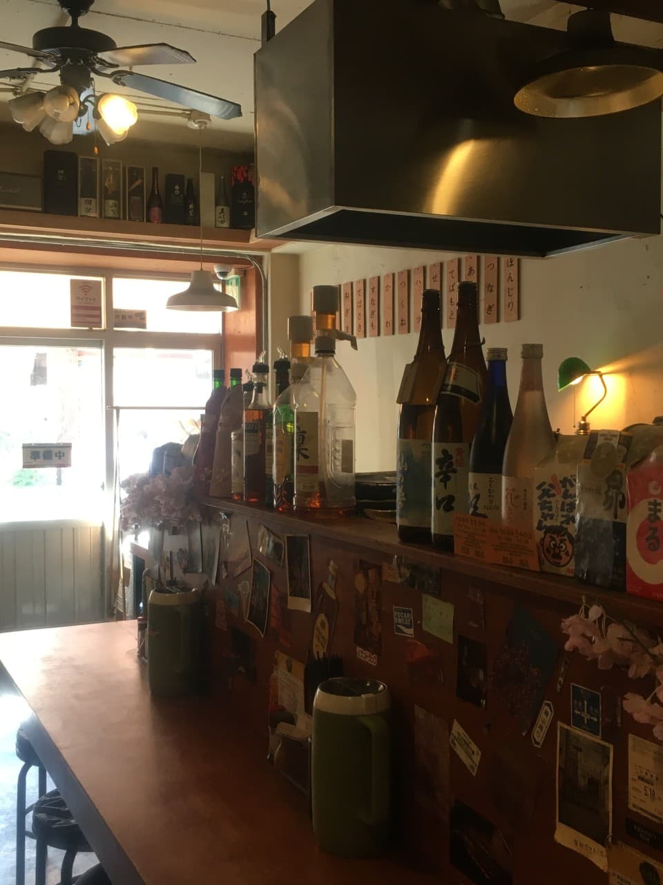 인천광역시 미추홀구 이자카야 야키토리 니센 인천 - 다찌석에 진열된 술병들과 혼술을 위한 바 테이블. 노란 조명이 비치는 나무 소재의 1인석 좌석 전경.
