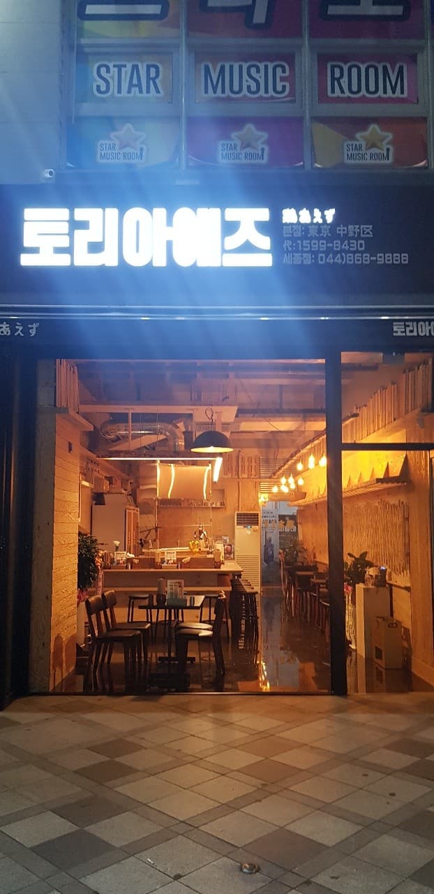 세종특별자치시 나성로 토리아에즈 세종점 이자카야의 주황색 조명 아래 1인 다찌석과 바 테이블. 목재 질감이 강조된 내부가 들여다보이는 혼술 분위기.
