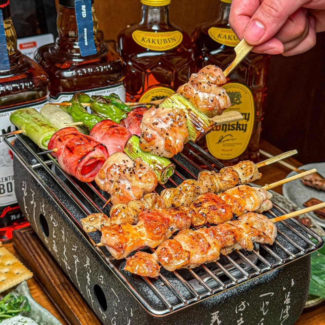 세종특별자치시 나성북로 숯토리 세종나성점 이자카야 다찌석의 1인 화로 구이. 노란 조명 아래 노릇한 닭꼬치와 대파의 질감, 배경에 진열된 위스키 병들이 배치된 혼술 상황.