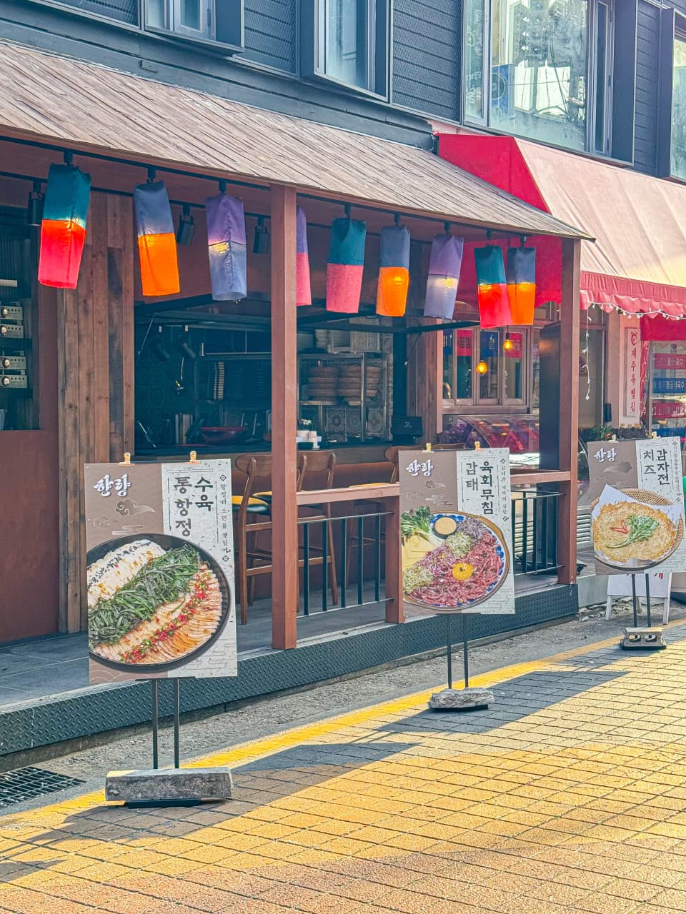 서울특별시 마포구 요리주점 한량 서울. 오색 등불 아래 1인 다찌석이 마련된 혼술 공간과 수육, 육회무침 메뉴 입간판이 나란히 설치된 외관.