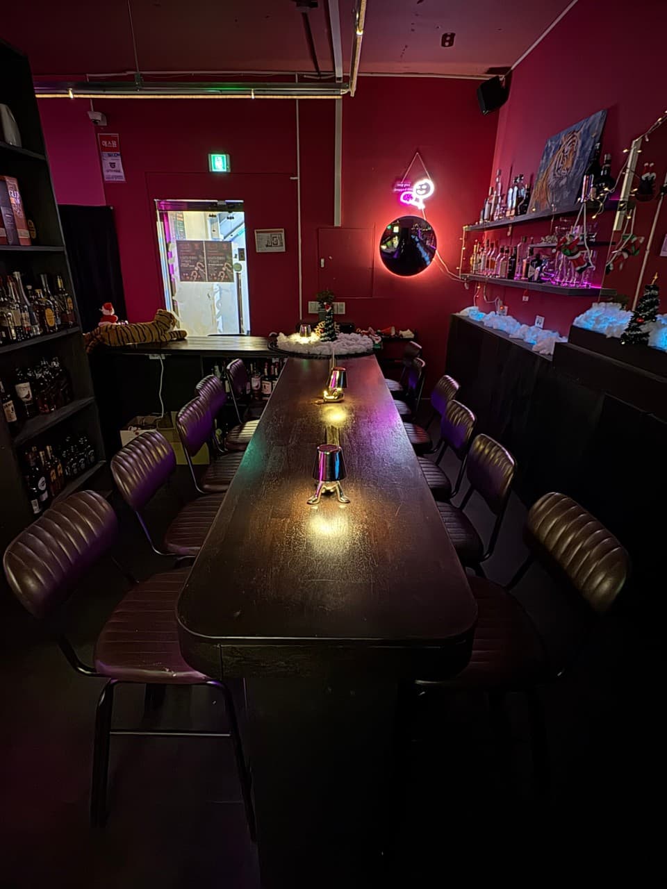 서울특별시 마포구 호랑이 라운지 서울 바(Bar) - 붉은 조명이 비치는 긴 나무 다찌석과 1인 가죽 의자. 벽면 선반을 채운 다양한 술병과 호랑이 장식물이 있는 혼술 환경