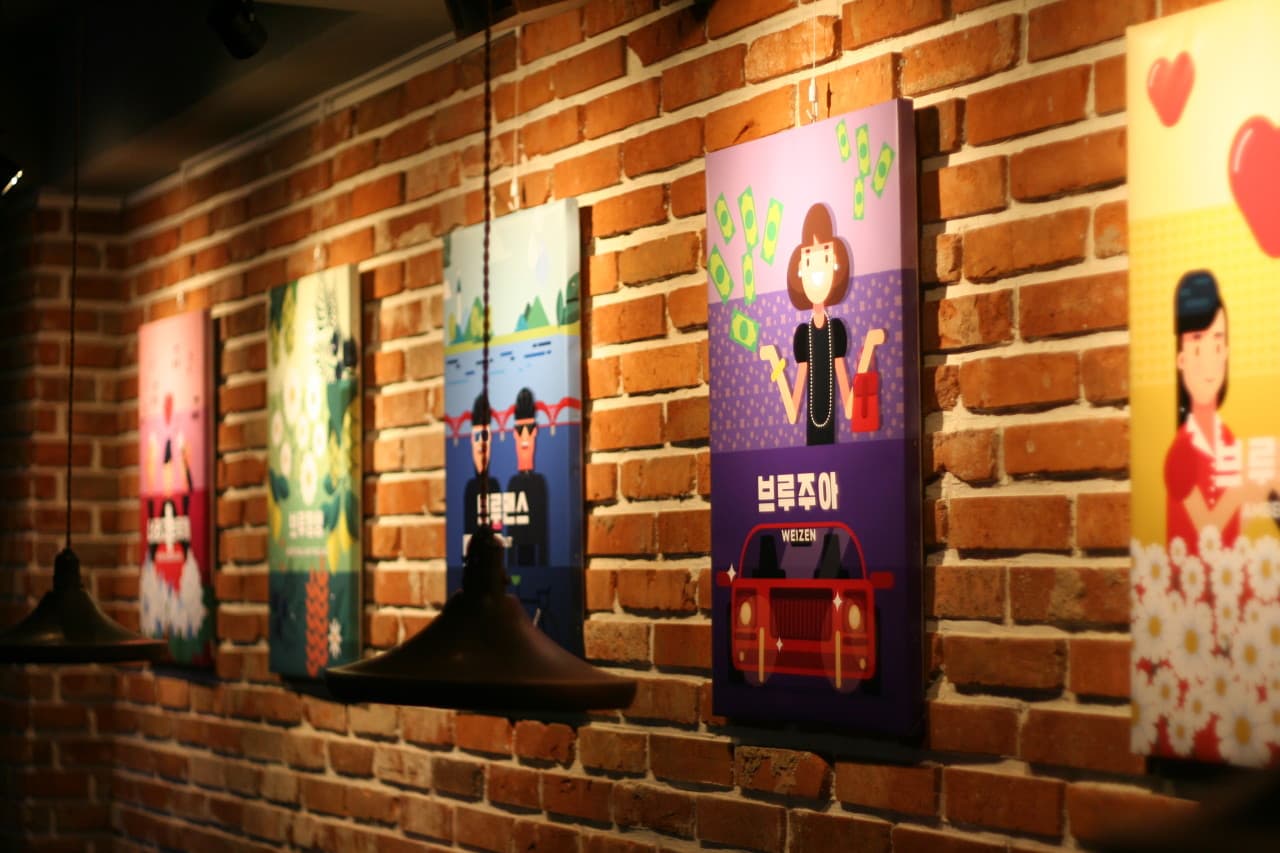 서울특별시 마포구 브루브루 서울 맥주 호프. 붉은 파벽돌 벽에 걸린 팝아트 포스터와 주황색 펜던트 조명이 비추는 혼술용 1인 다찌석 상단 인테리어.
