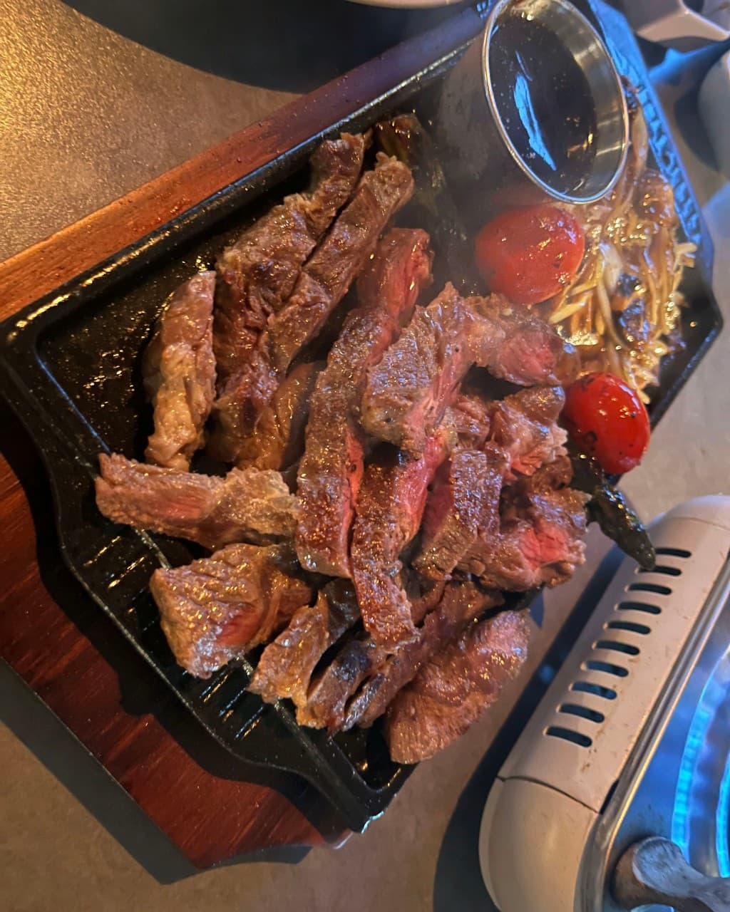 대전광역시 유성구 바시트 대전 이자카야 다찌석 조명 아래 무쇠 철판에 담긴 스테이크와 구운 토마토. 붉은 단면의 고기와 소스가 차려진 1인 혼술 상황.