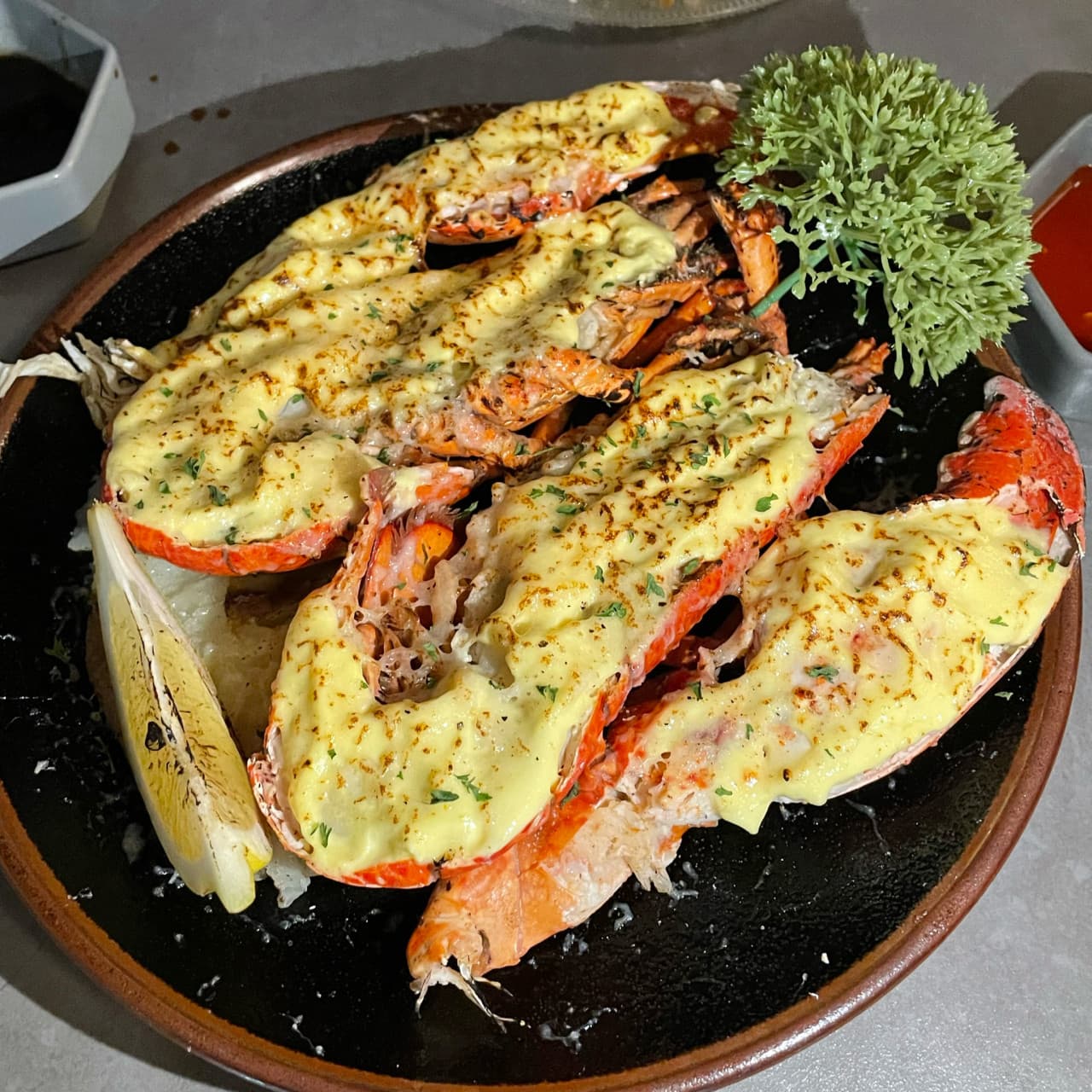 대전광역시 유성구 바시트 대전 이자카야의 다찌석 조명 아래 차려진 1인 치즈 랍스터 구이. 노릇하게 구워진 치즈의 질감과 레몬이 곁들여진 혼술 메뉴의 구성을 상세히 묘사함.