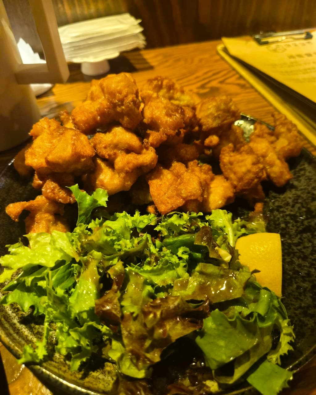 대전광역시 서구 마포십번 갈마본점 이자카야의 황색 조명 아래 나무 다찌석. 바삭한 식감의 치킨 가라아게와 샐러드 접시가 놓인 1인 혼술 상황을 묘사함.