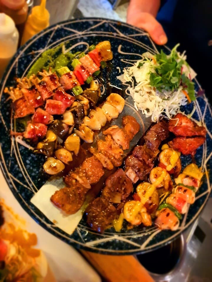 대전광역시 중구 해마직화구이 대전 이자카야 다찌석 노란 조명 아래 놓인 윤기 나는 모둠 꼬치구이와 양배추 샐러드 구성의 혼술 상차림