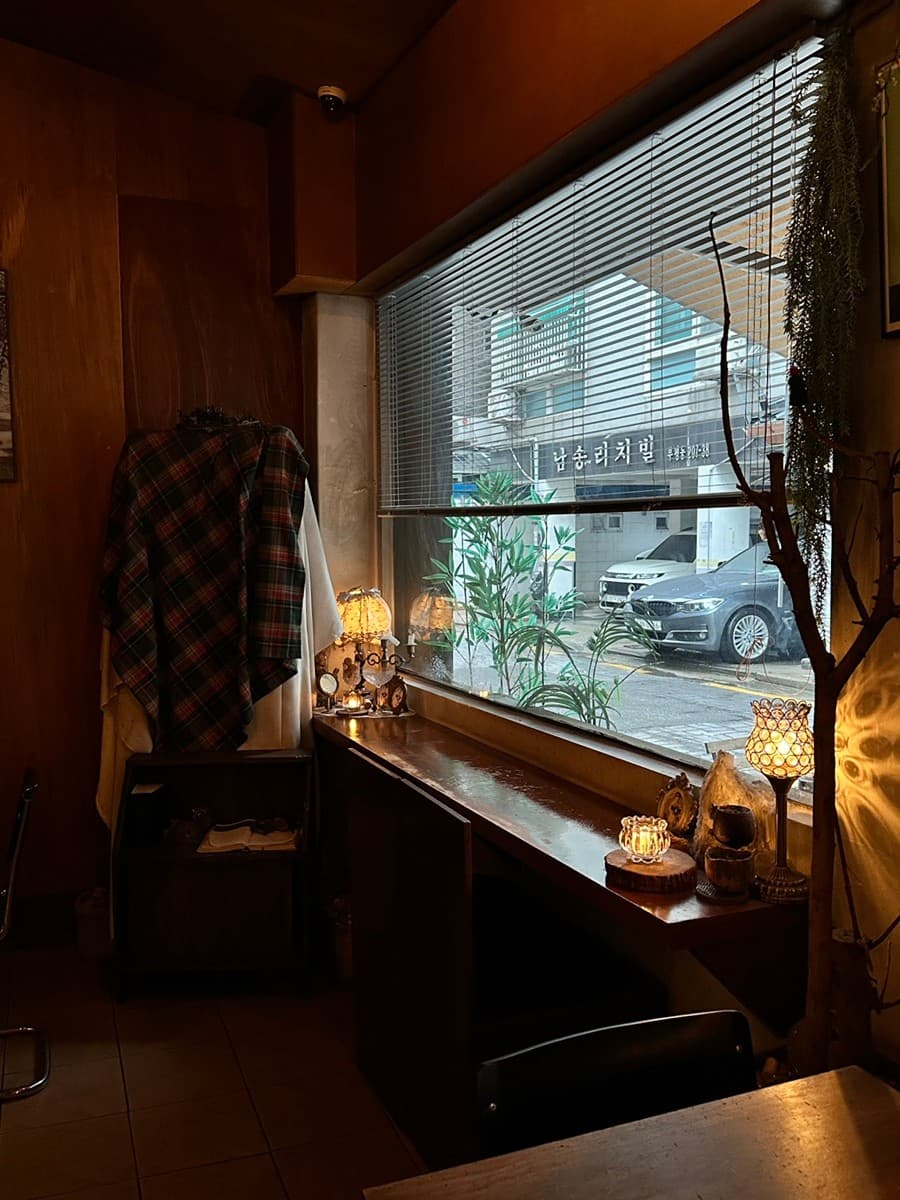인천광역시 부평구 15평 인천 바(Bar)의 창가 1인 다찌석. 주황색 조명과 목재 테이블, 소품들이 배치된 실내에서 블라인드 사이로 외부 전경이 보이는 혼술 상황.