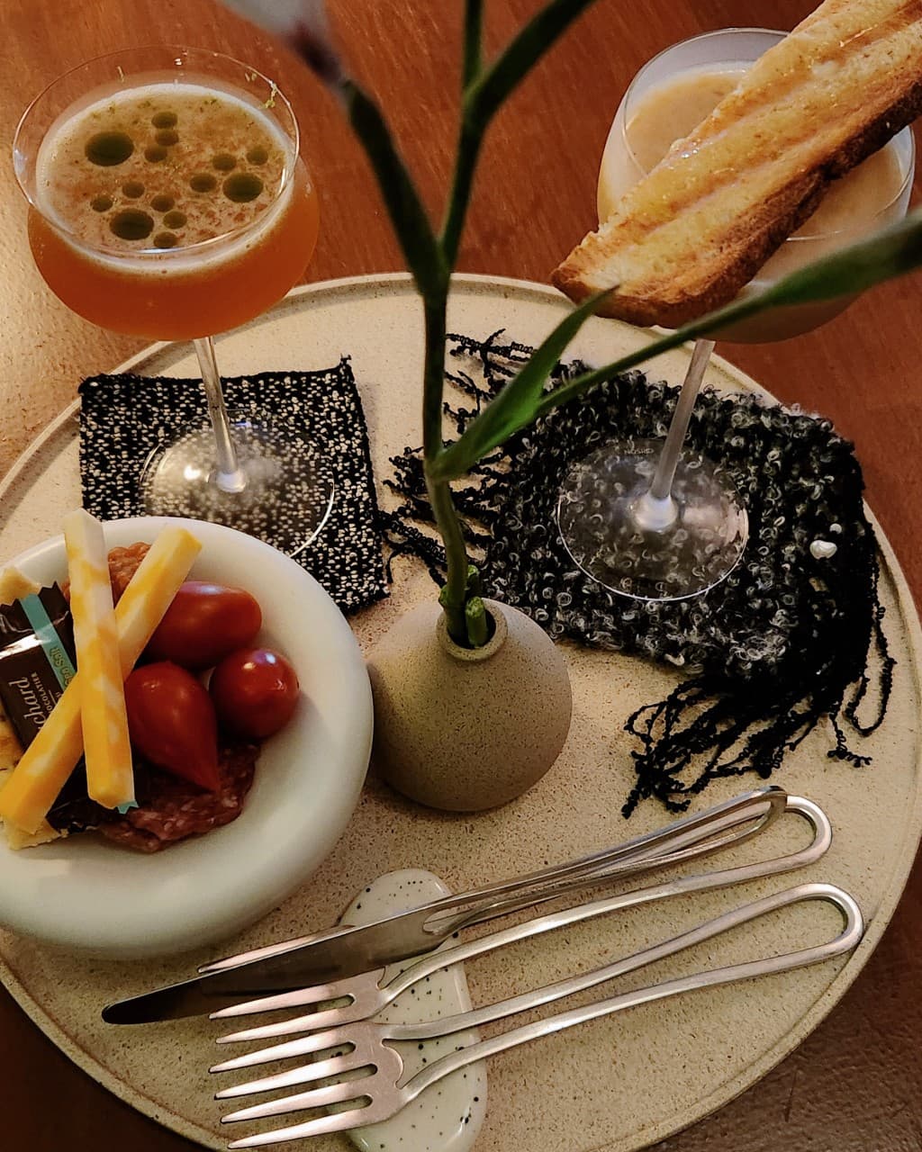인천광역시 부평구 홀로 낮과밤 인천 이자카야 1인 다찌석. 주황빛 칵테일과 치즈, 방울토마토가 담긴 원형 트레이. 낮은 조도 아래 금속 식기와 작은 화분이 놓인 혼술 테이블.