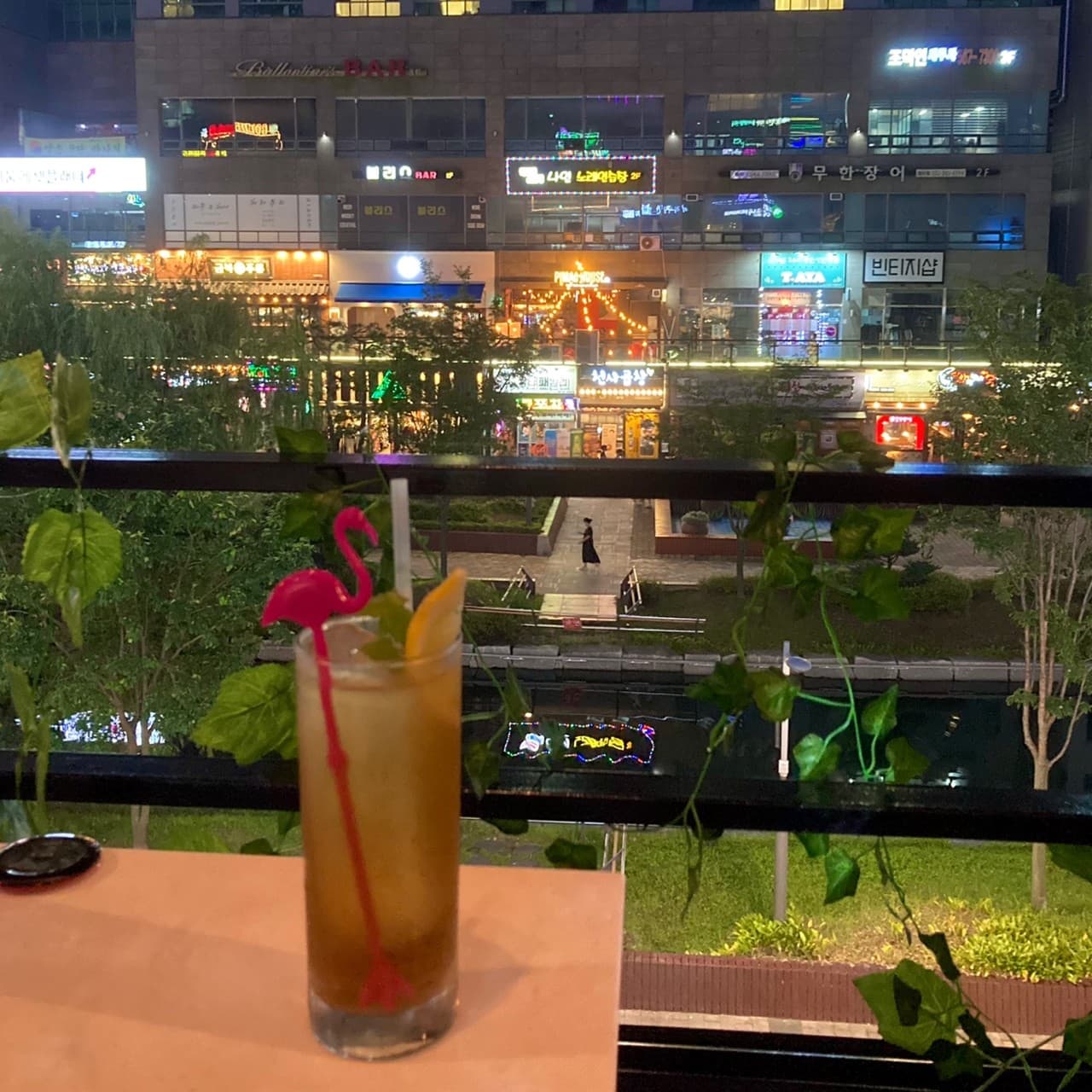 인천광역시 서해구 바(Bar) 러시안블루 인천 테라스에서 즐기는 혼술. 핑크색 플라밍고 머들러와 레몬이 담긴 하이볼 뒤로 화려한 상가 조명과 수변 산책로가 보이는 야경.