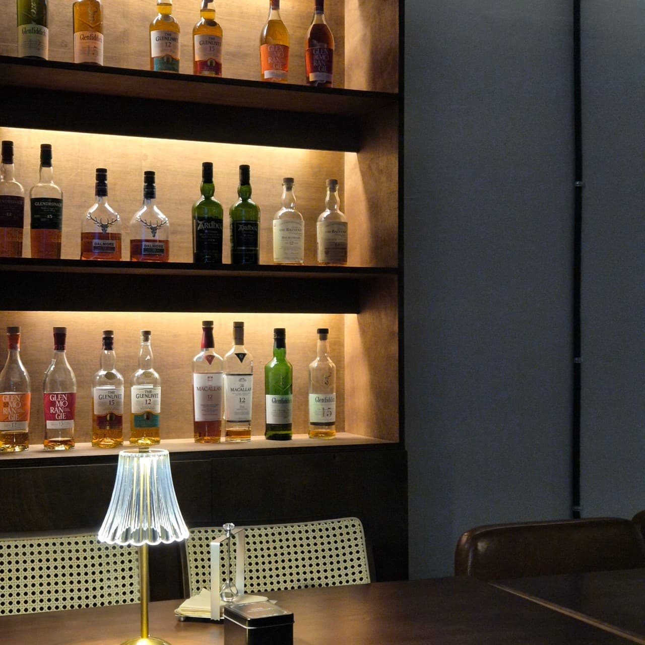 인천광역시 부평구 꼼바혼술바 인천부평점 인천 바(Bar). 진열된 위스키 병과 하단 조명, 다찌석 테이블 위 스탠드 램프가 배치된 1인 혼술 전용 좌석
