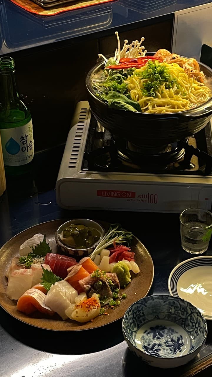 인천광역시 남동구 이자카야결 인천 다찌석 위 선명한 질감의 1인 모둠 사시미와 해물 나베 및 소주. 낮은 조도 아래서 혼자 식사하는 혼술 상황을 보여줌.