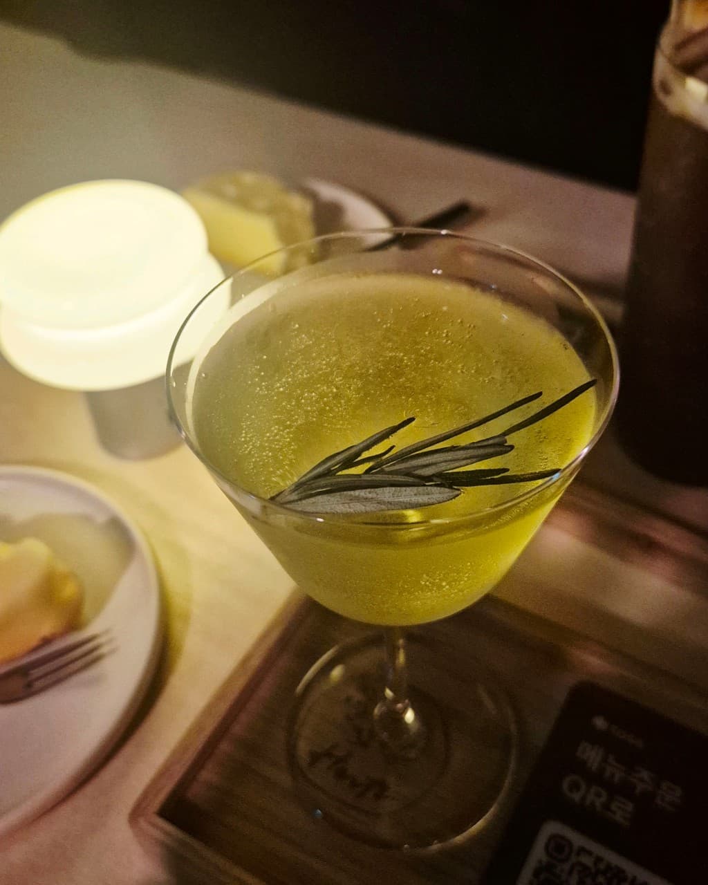 인천광역시 부평구 헤르츠 혼술바 부평점 인천 바(Bar). 황색 조명이 비치는 1인석 다찌에 놓인 로즈마리 칵테일과 나무 트레이 위 안주. 혼자 술을 즐기는 상황.