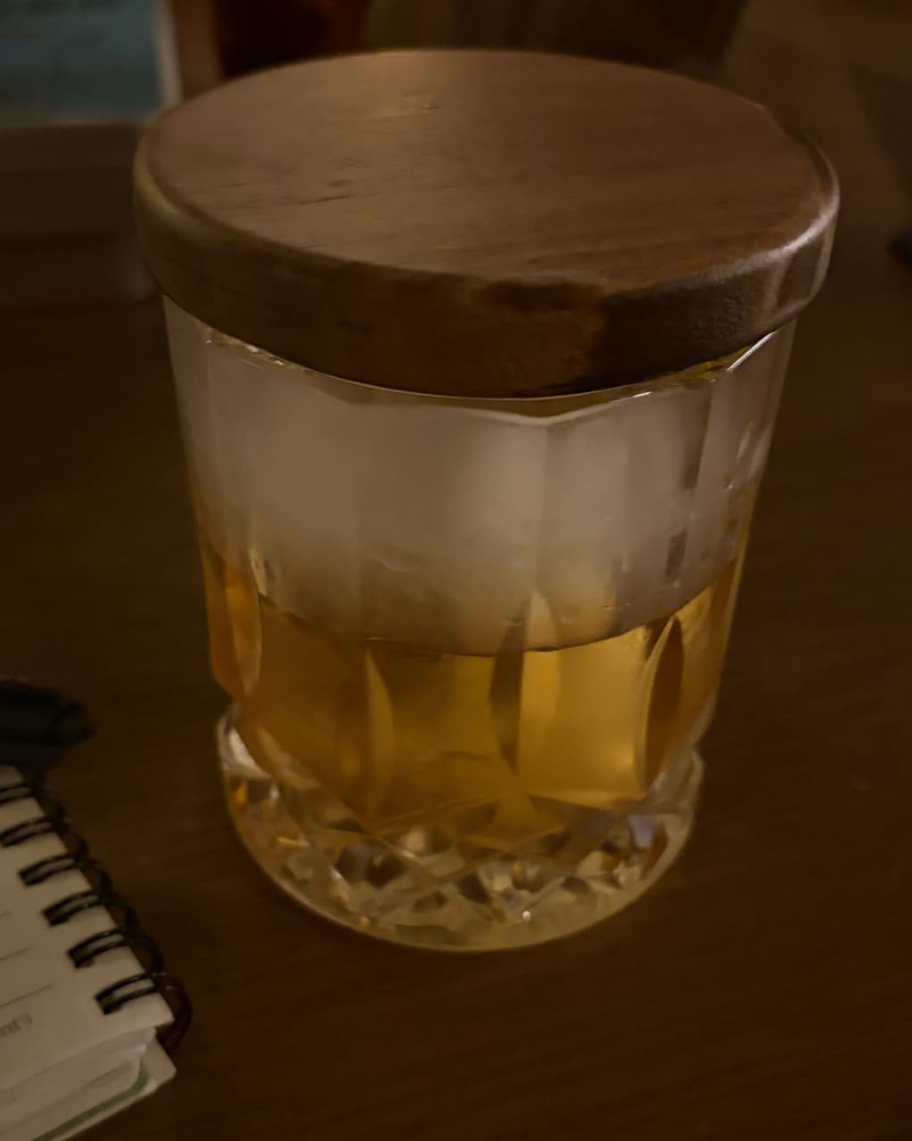 인천광역시 남동구 곁혼술바 구월점 인천 바(Bar) 다찌석의 어두운 조명 아래 나무 뚜껑을 덮은 술잔과 수첩이 놓여 혼술하는 상황을 보여줌.