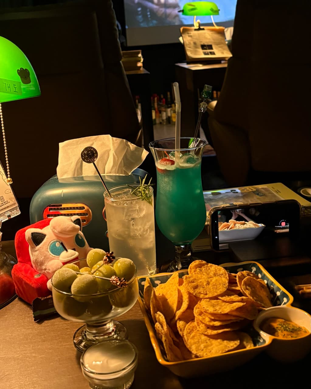 전남광주통합특별시 여수시 여수골방 전남 바(Bar) 초록색 조명 아래 1인 좌석에 놓인 칵테일과 나초. 혼술을 하며 스마트폰 영상을 시청하는 다찌석 상황
