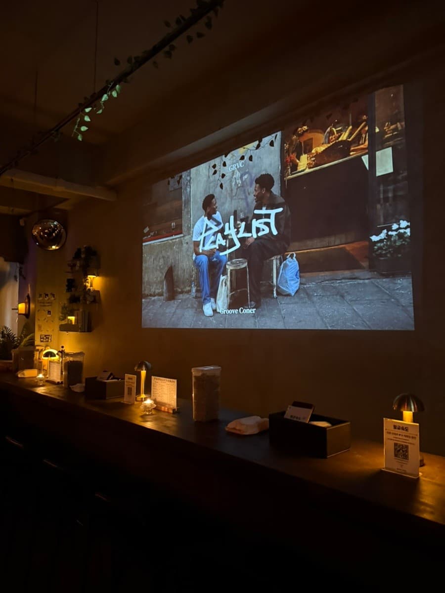 전남광주통합특별시 동구 광주혼술바 평균속도 동명점 전남 바(Bar) 내부. 빔프로젝터 영상 아래 노란 조명이 놓인 1인 다찌석이 배치된 혼술 공간.