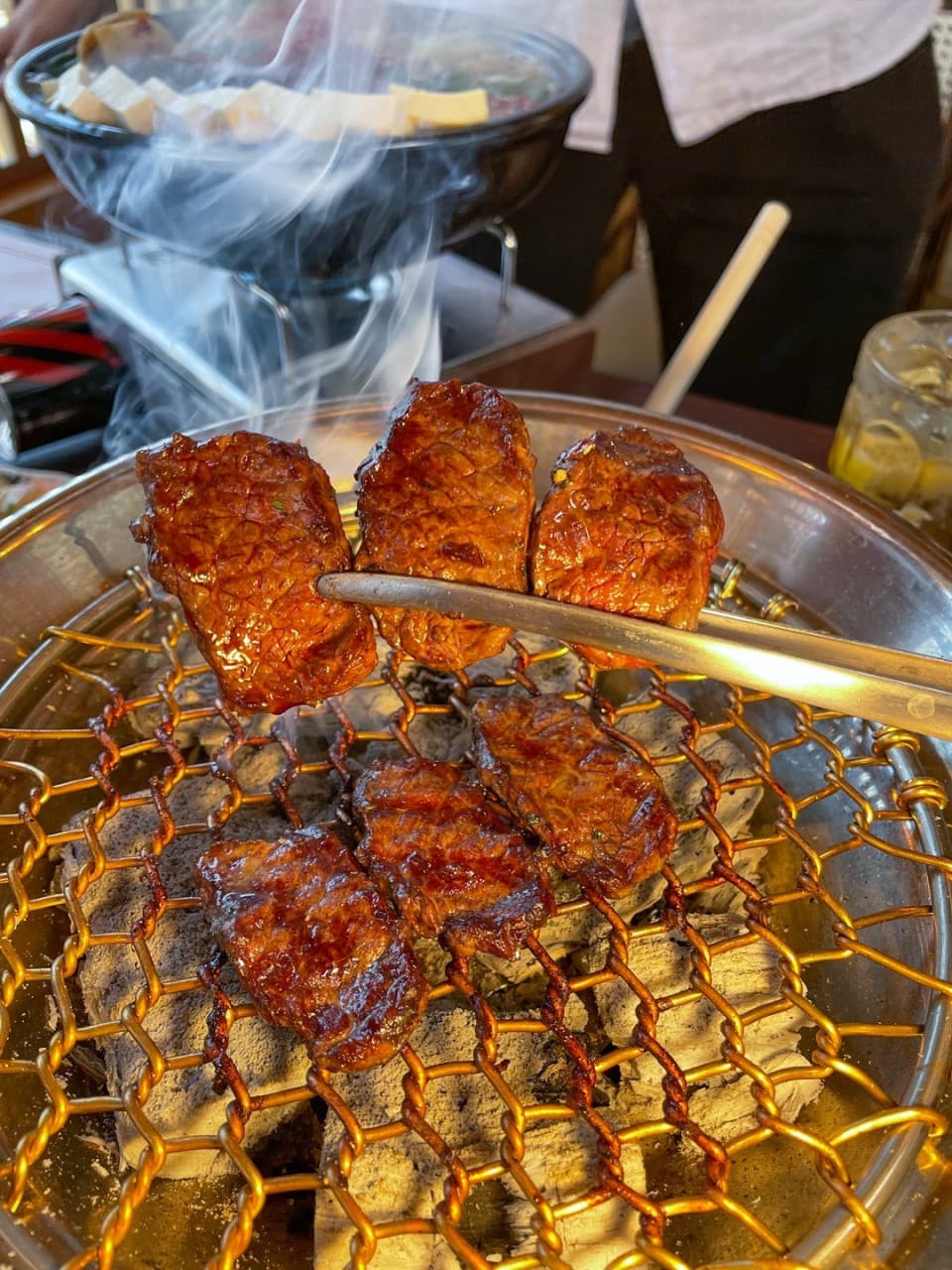 경상북도 경주시 모모치준 황남 경북 이자카야 다찌석 1인 혼술 상황. 숯불 화로 위 연기가 피어오르는 고기 질감과 나베, 하이볼이 차려진 조명 아래 테이블.