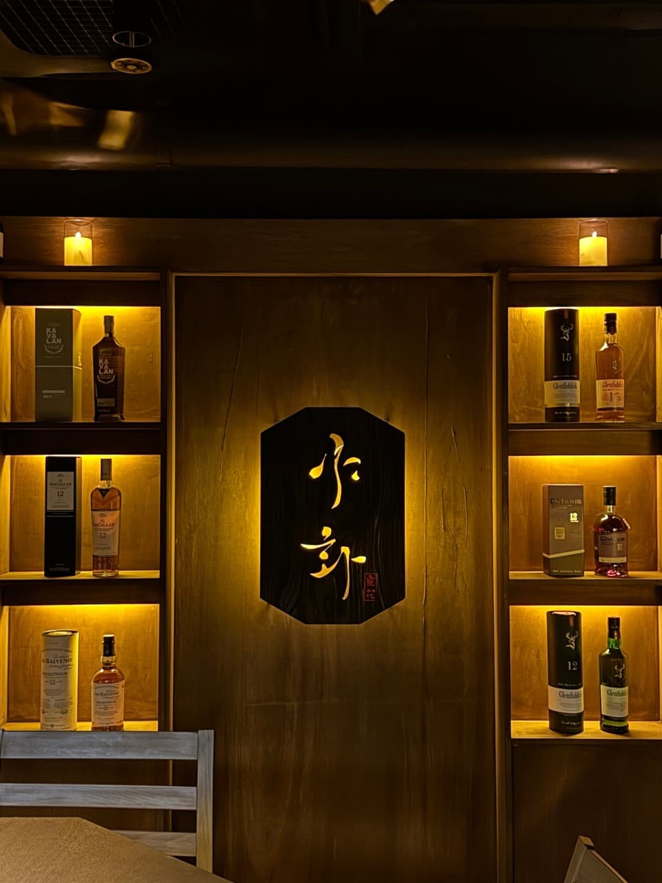 전남광주통합특별시 서구 야화 혼술바 광주상무점 전남 바(Bar)의 노란 조명 아래 진열된 위스키. 원목 벽면과 1인 다찌석이 마련되어 혼술에 집중할 수 있는 공간 구성을 보여줌.