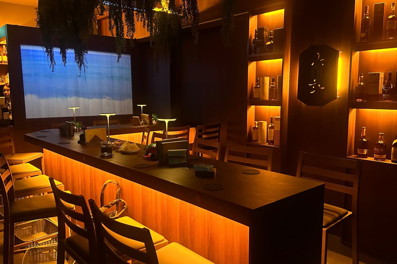 전남광주통합특별시 서구 야화 혼술바 광주상무점 전남 바(Bar) 내부. 주황빛 간접 조명이 비치는 긴 다찌석과 1인 의자, 선반 위 양주병들이 위치한다. 카운터 위에는 안주 접시와 술잔이 놓인 혼술 상황.
