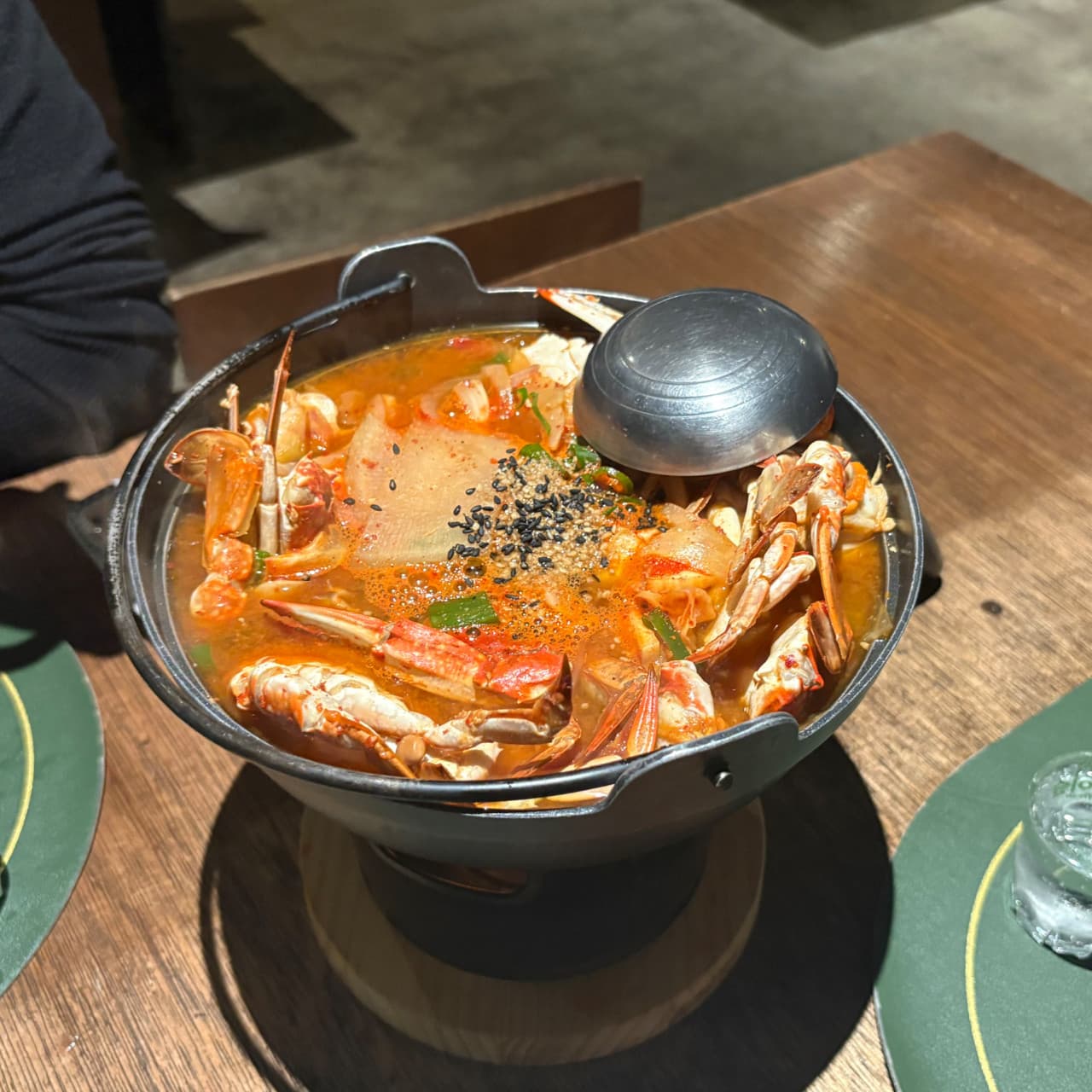 경상북도 경주시 요리주점 안다미로 경북 나무 테이블 위 1인 혼술 차림. 꽃게가 가득 담긴 무쇠 솥과 초록색 매트 위 소주잔이 놓인 다찌석의 상황.