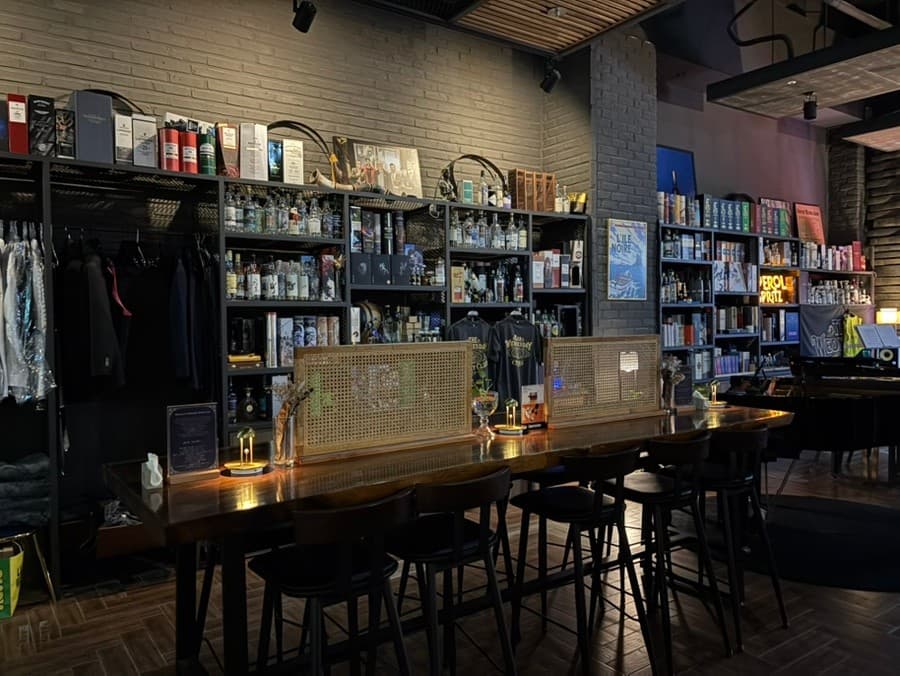 대전광역시 유성구 웬즈데이위스키클럽 대전 바(Bar). 낮은 조도 아래 원목 다찌석과 칸막이가 설치된 1인 좌석. 벽면의 수많은 위스키 병들 사이에서 혼술을 즐기는 공간.